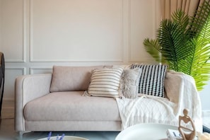 A beige sofa with patterned cushions, a white throw blanket, and a wooden sculpture on a table. - CUBIC BOTANICAL BY FEEL HOME (Kuala Lumpur)