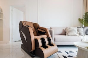 Un salon moderne avec un fauteuil massant, un canapé agrémenté de coussins à motifs et une petite table ronde.