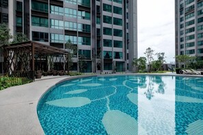 Une piscine dont le fond est recouvert de carreaux formant un motif géométrique, entourée d’une terrasse en béton et agrémentée d’un espace salon abrité.