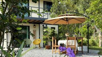 An outdoor patio with a table and chairs, surrounded by potted plants and a large umbrella.
