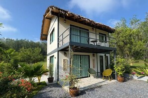 A two-story house with a balcony, surrounded by a garden with potted plants and a gravel driveway. - Uma Valley Homestay - Relaxing home with private garden (Sadao)