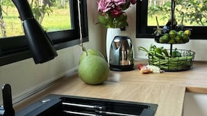Eine Küchenarbeitsplatte mit Obstkorb, einer Birne, einer Blumenvase und einem Wasserkocher.