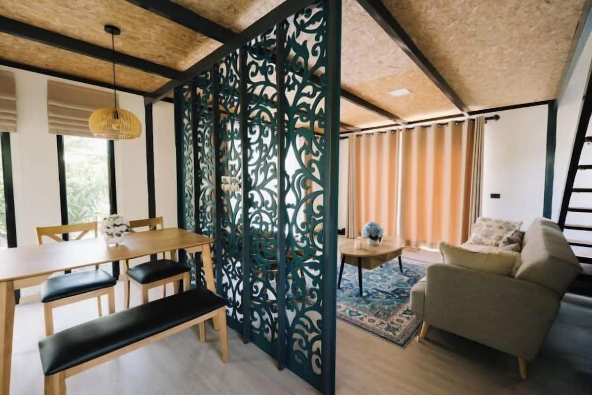 A room with a wooden dining table, benches, a sofa, and a decorative partition with intricate designs.