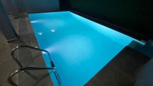 A swimming pool with a clear blue water surface, a metal ladder, and a dark surrounding wall. - Nirosha Guest House (Galle)