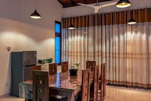 A dining area with a wooden table, chairs, a refrigerator, and a television. - Nirosha Guest House (Galle)
