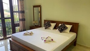 A neatly made bed with towels and pillows, a wooden headboard, a nightstand with a lamp, and a large mirror. - Nirosha Guest House (Galle)