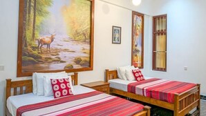 A room with two wooden beds, each with a red-striped bedspread and white pillows. A large painting of a deer in a forest is on the wall above the beds. - Nirosha Guest House (Galle)