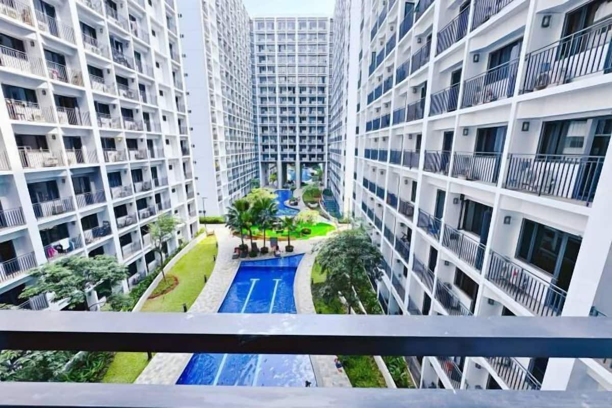A high-rise residential building with multiple balconies, a central courtyard with a swimming pool, and surrounding greenery.