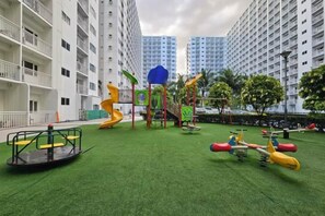 A playground with various play equipment, surrounded by a grassy area and tall residential buildings. - Shore Residences MOA staycation (Pasay)