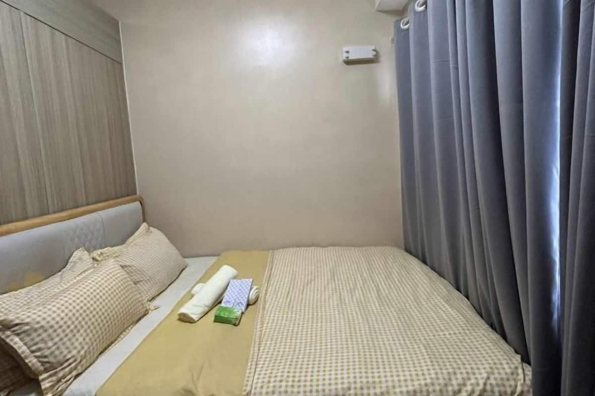 A hotel room with a bed, a pillow, a blanket, a small table, and a curtain.