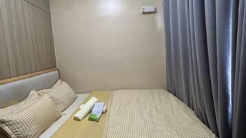 A hotel room with a bed, a pillow, a blanket, a small table, and a curtain.