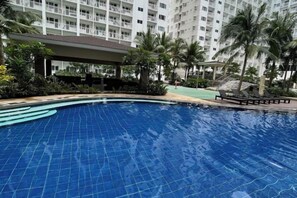 A swimming pool with a tiled surface, surrounded by a landscaped area with palm trees and a covered walkway. - Shore Residences MOA staycation (Pasay)