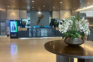 A reception area with a reception desk, a digital screen, and a decorative vase with flowers. - Shore Residences MOA staycation (Pasay)