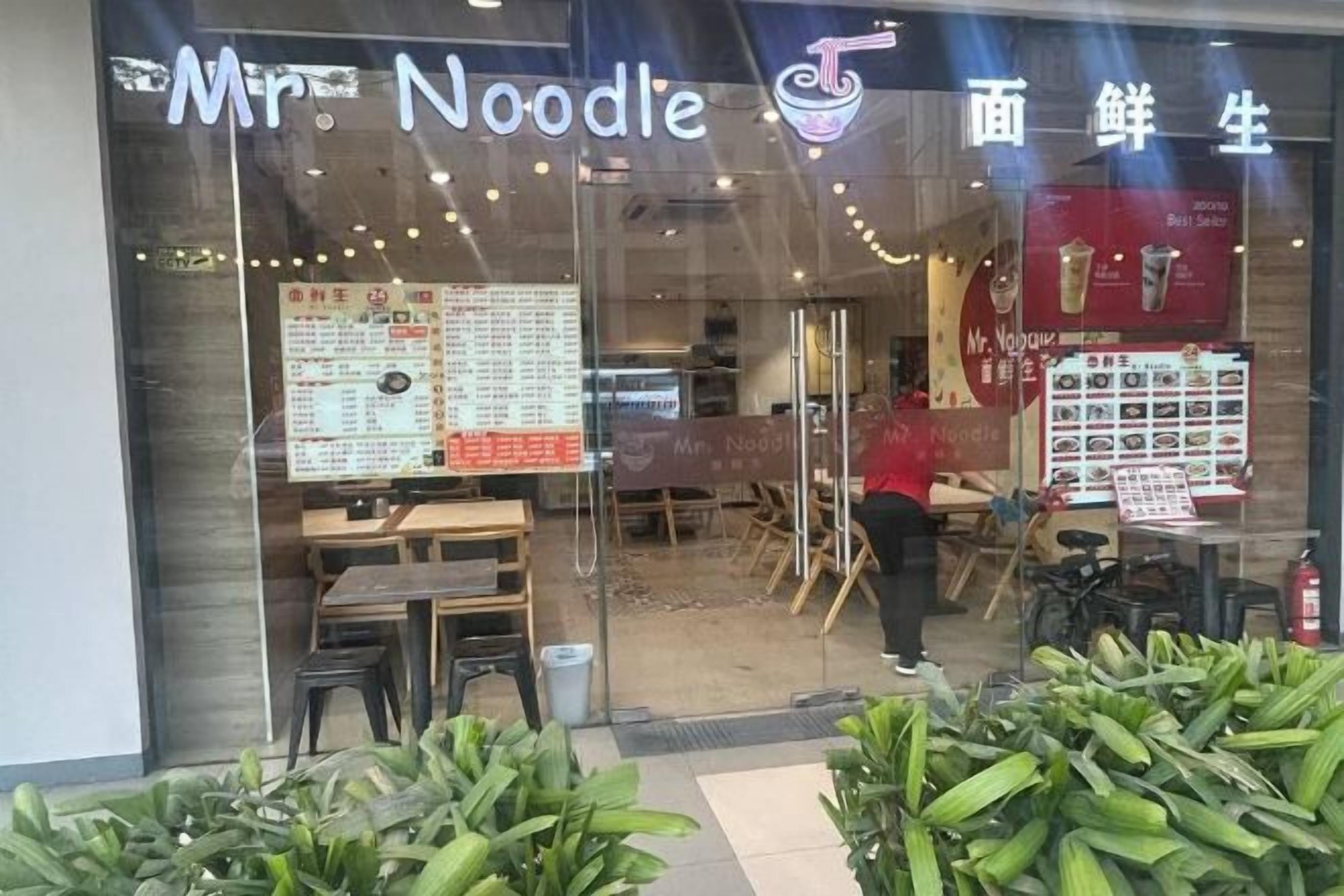 A restaurant named 'Mr. Noodle' with a menu board and seating area visible through the glass.