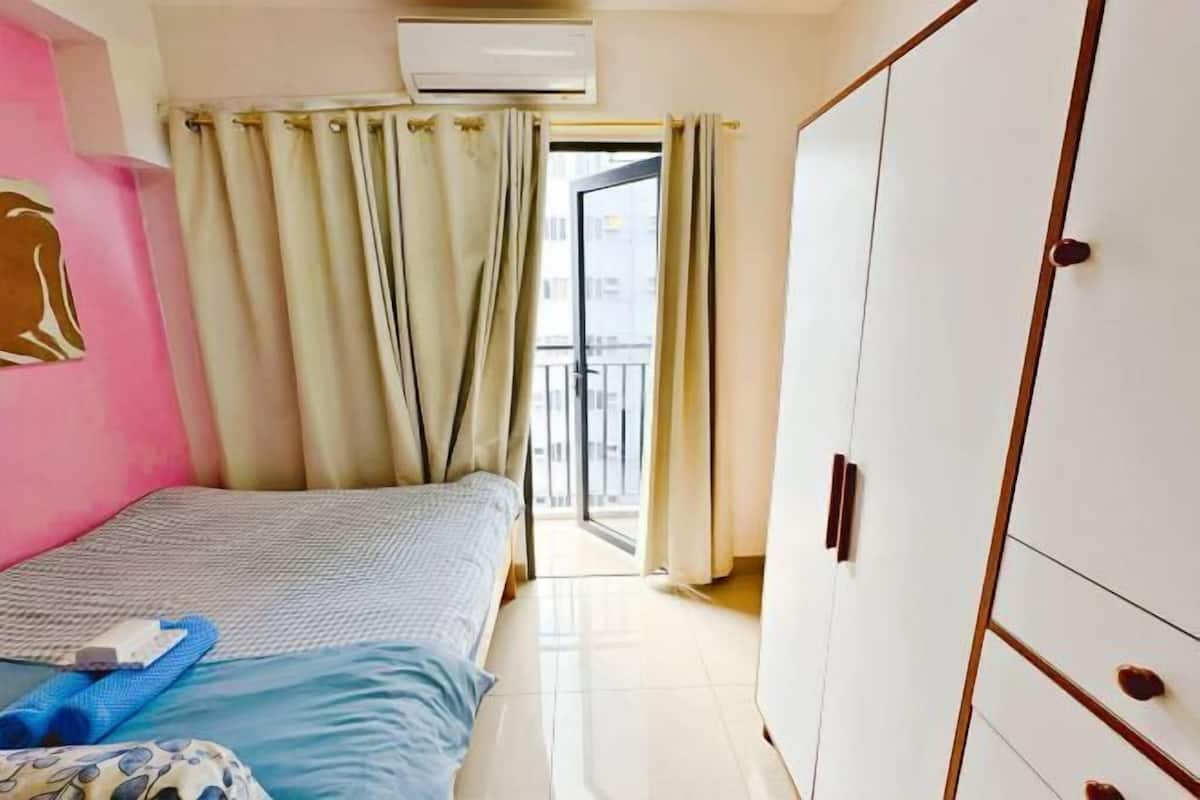 A bedroom with a bed, a wardrobe, a window with curtains, and an air conditioning unit.