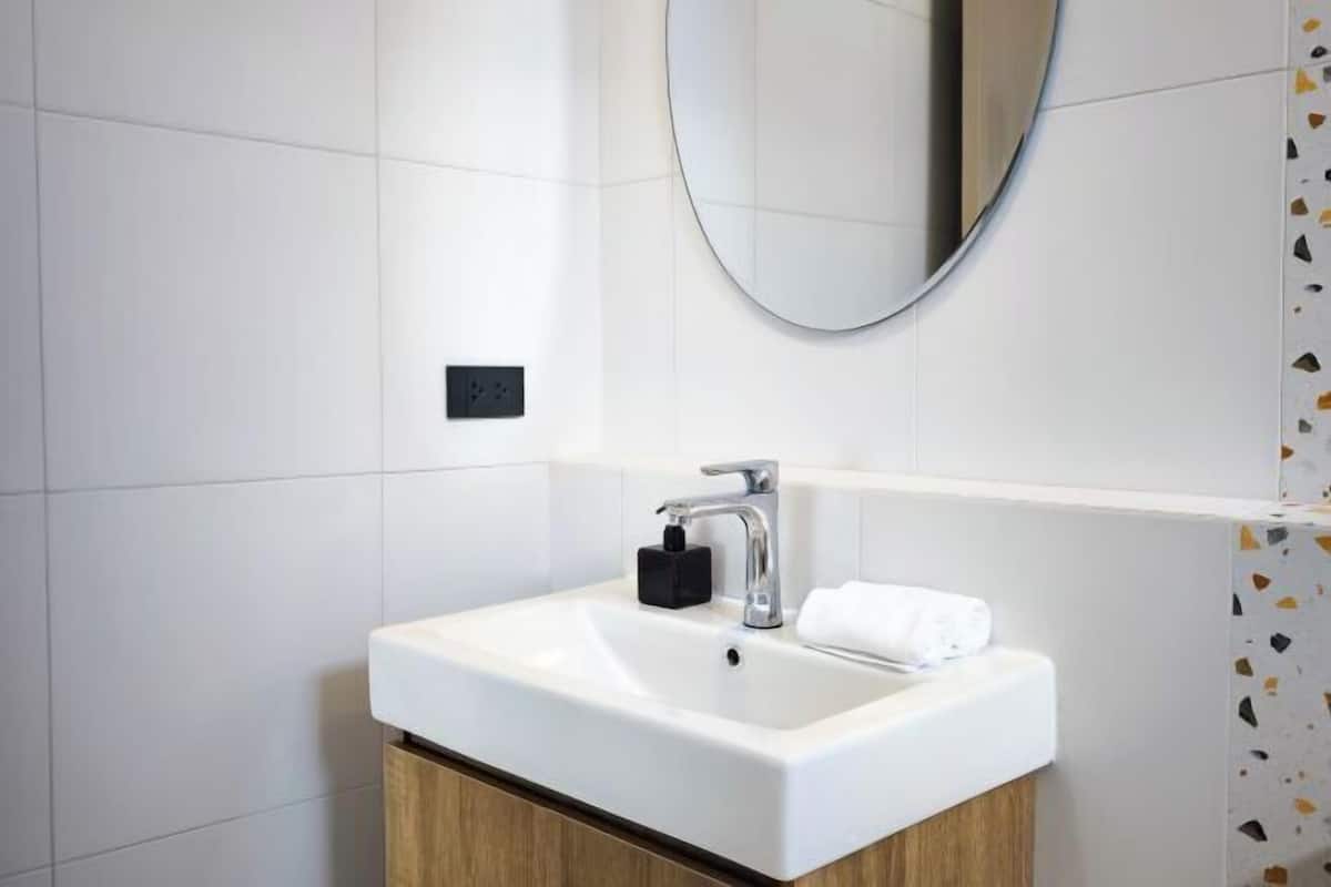 Un baño moderno con un lavamanos blanco, un espejo y un perchero para toallas.