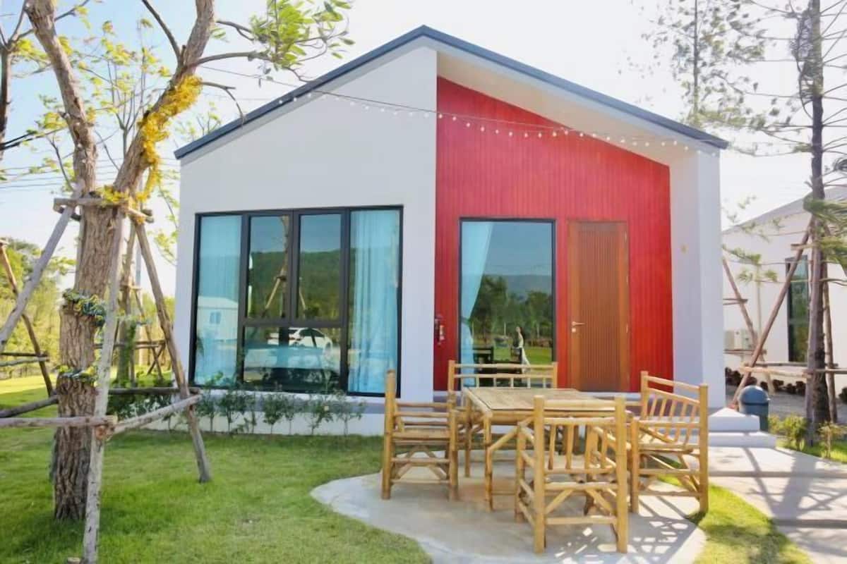 Un edificio moderno con grandes ventanales, fachada roja y una mesa y sillas de madera al frente.