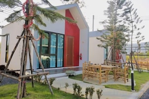 Un edificio moderno con puerta roja, entrada de vidrio y un pequeño espacio al aire libre con mesas y sillas.