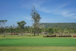 Un campo de golf con cielo despejado, árboles y un paisaje montañoso al fondo.