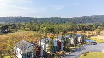A row of modern cabins with large windows, set in a rural landscape with a clear road and distant hills.