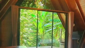 Una habitación con un gran ventanal corredero que da a un balcón con abundante vegetación.