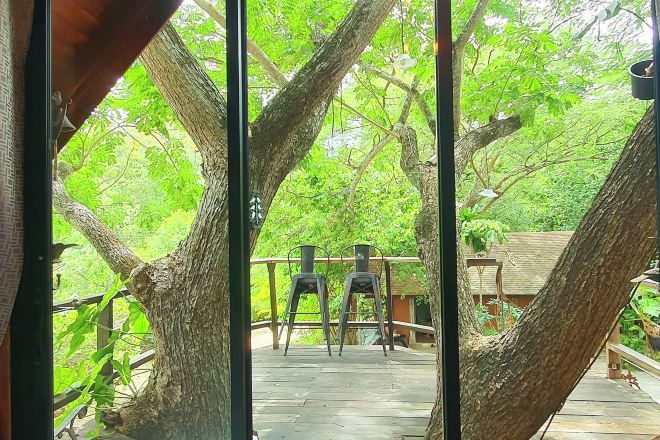 A wooden deck with two metal chairs and a table, surrounded by trees.