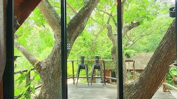 A wooden deck with two metal chairs and a table, surrounded by trees.