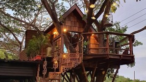 Una casa en árbol con varios niveles, barandas de madera y luces colgantes.