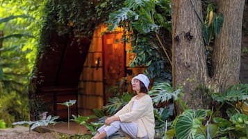 A person sitting on a stone bench in a lush garden with a wooden structure in the background.