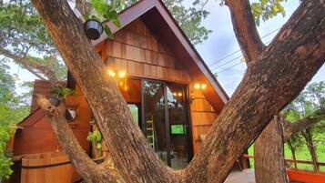 A treehouse with a wooden exterior, large windows, and a ladder leading up to the entrance.