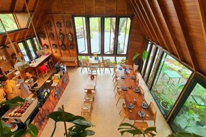 A dining area with a long wooden table, chairs, and a bar counter with food and drinks. - Kenaray Farmstay Riverside (Kaeng Krachan)