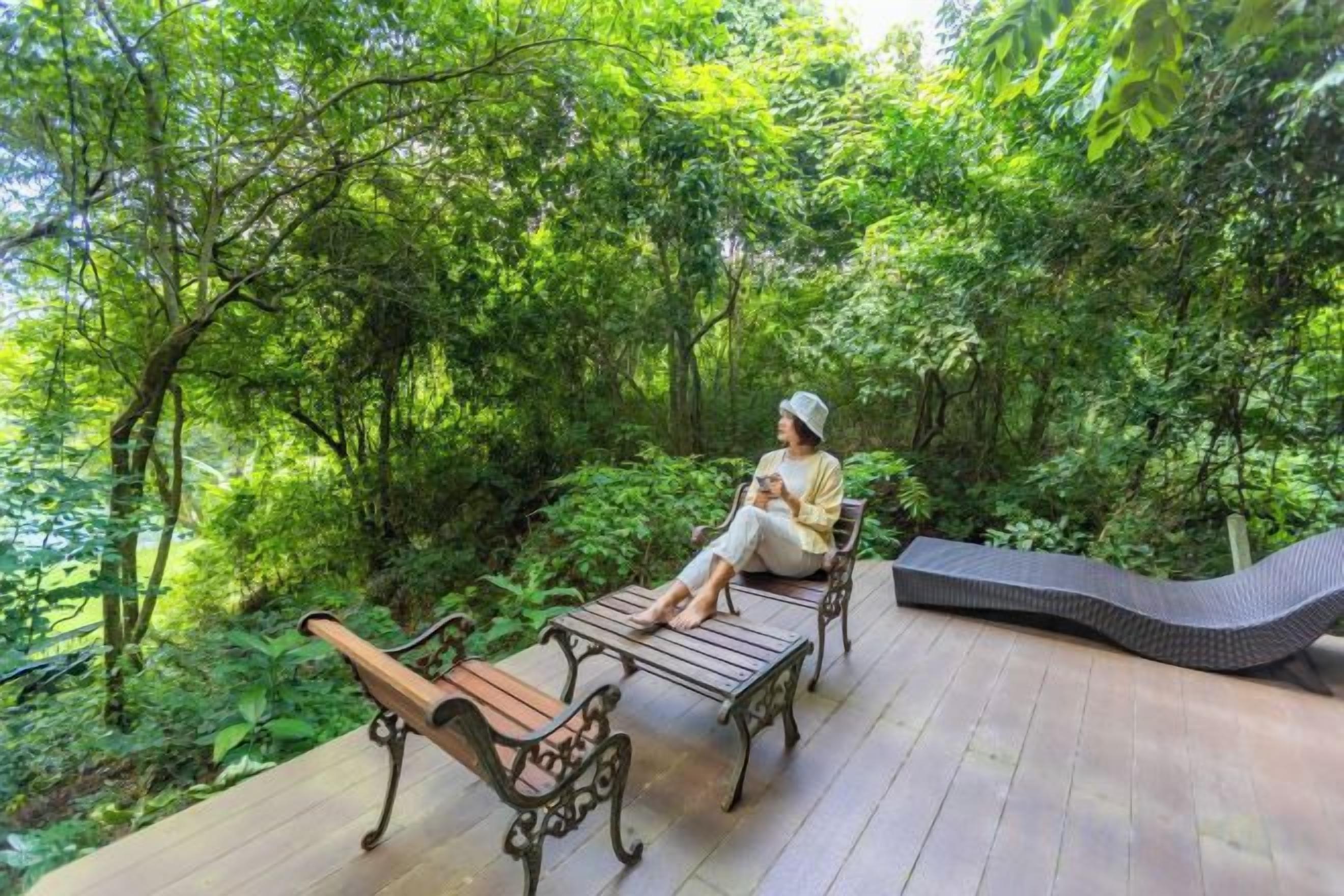 A wooden deck with two benches and a curved bench, surrounded by lush greenery.