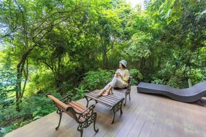 A wooden deck with two benches and a curved bench, surrounded by lush greenery. - Kenaray Farmstay Riverside (Kaeng Krachan)
