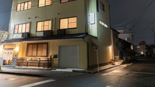 Un immeuble à plusieurs étages, doté d’une façade recouverte de carreaux, d’une porte de garage visible et d’un petit espace porche agrémenté d’une clôture.