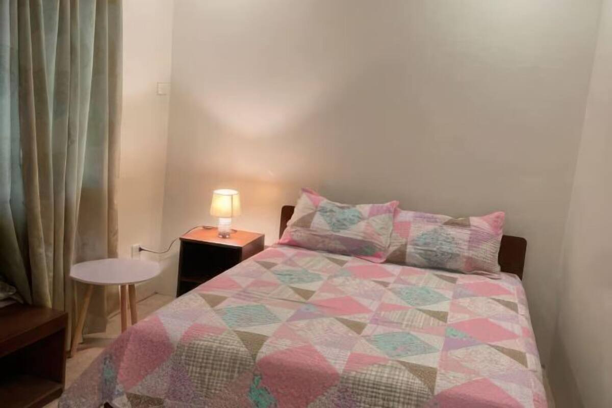 Une petite chambre à coucher, bien rangée, avec un lit, une table de chevet dotée d’une lampe et une chaise.