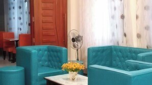 A room with teal upholstered sofas, a small table with a vase of yellow flowers, a fan, and a wooden door. - Sunnyside Hotel (Santo Tomas)