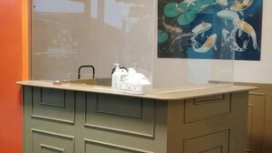 A reception desk with a glass partition, a painting of aquatic life on the wall, and a counter with toiletries. - Sunnyside Hotel (Santo Tomas)