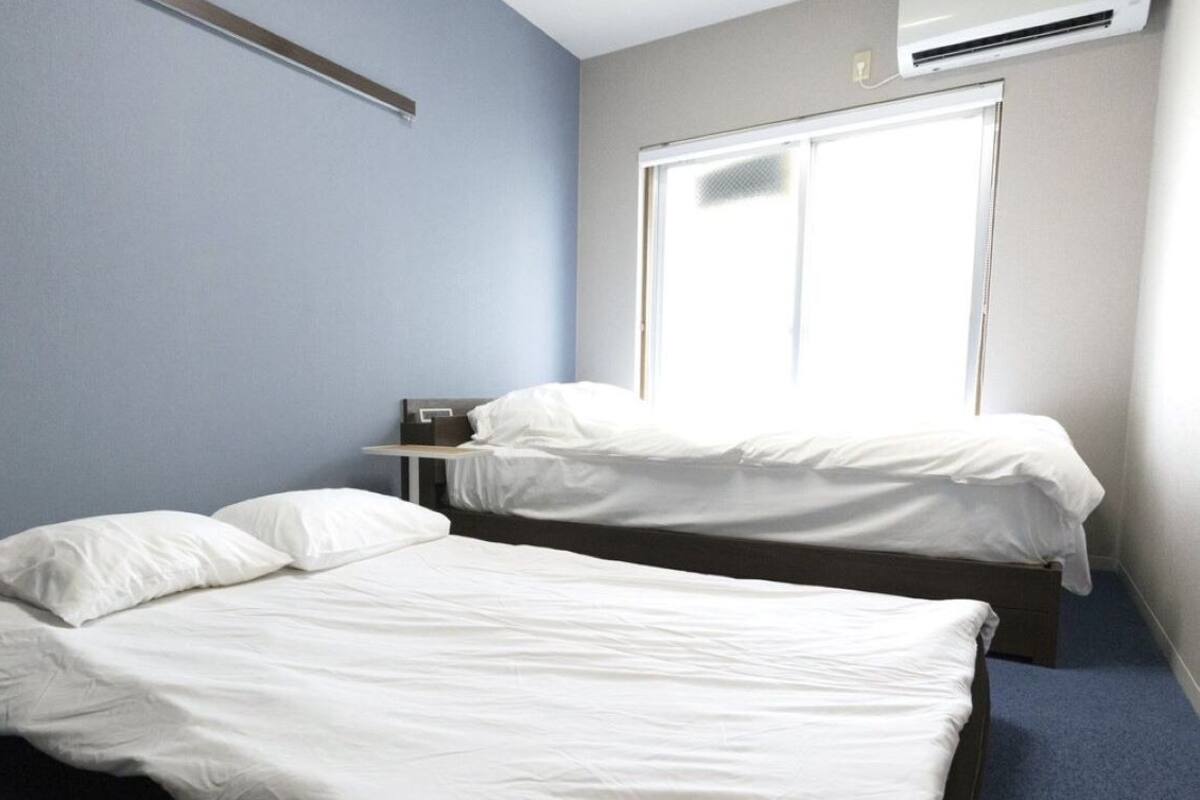 Una habitación con dos camas, una ventana y aire acondicionado instalado en la pared.