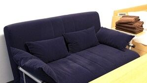 Ein dunkelblaues Sofa mit zwei Kissen, ein Holztisch mit gefalteten Handtüchern und eine weiße Wand.