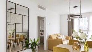 A modern living room with a dining area, featuring a large mirror, a sofa, a coffee table, and a dining table with chairs.