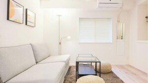 A modern living room with a sofa, a glass coffee table, a floor lamp, and a window with blinds. - Oyama Pantheon (Tokyo)