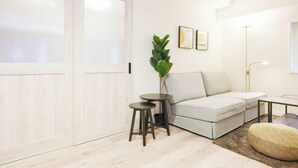A modern living room with a sofa, two small round tables, a potted plant, and a large window. - Oyama Pantheon (Tokyo)