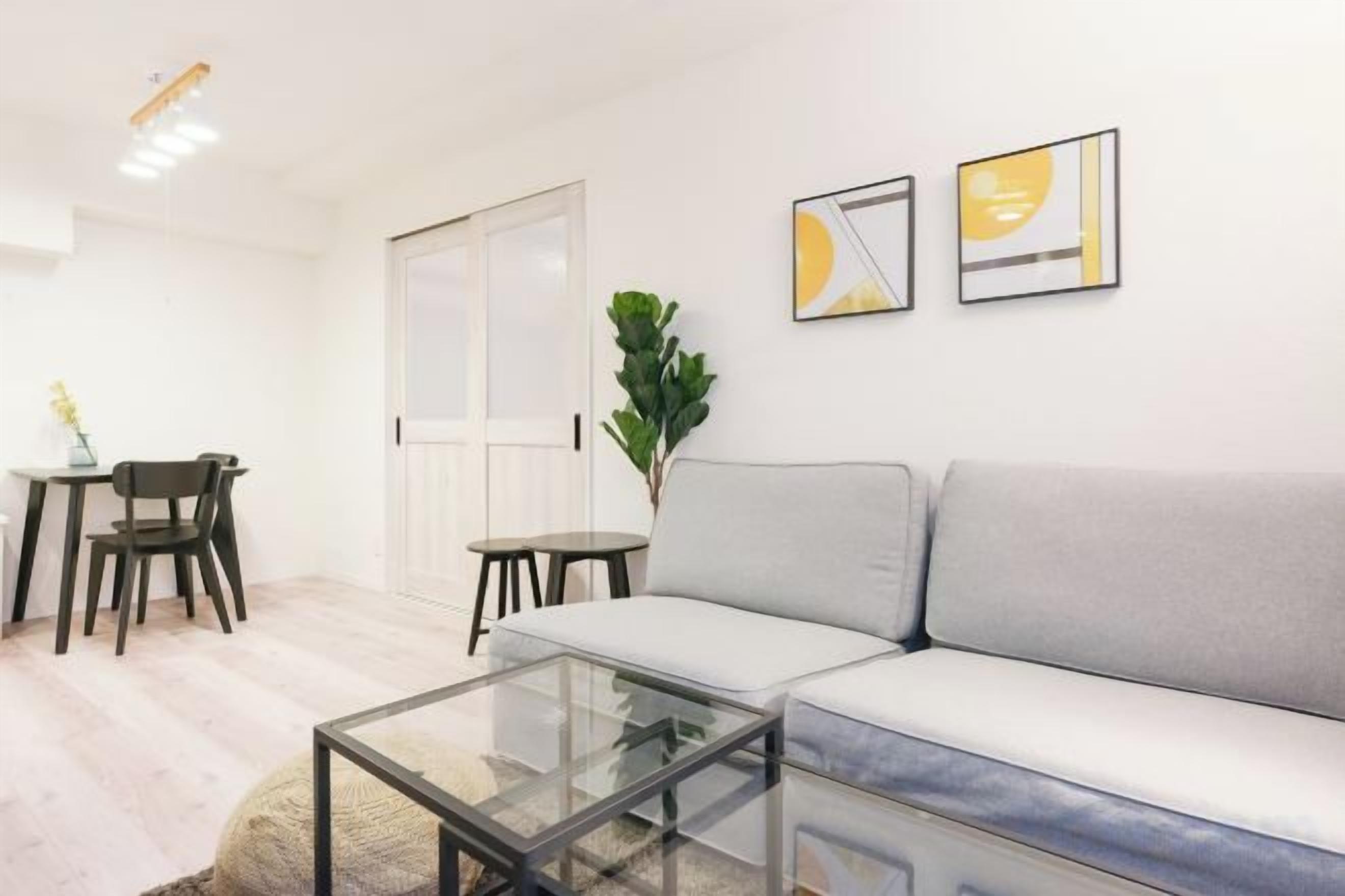 A modern living room with a sofa, a glass coffee table, and a dining area with chairs and a table.
