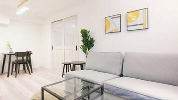 A modern living room with a sofa, a glass coffee table, and a dining area with chairs and a table.