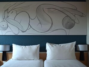 A hotel room with a large abstract painting on the wall, two white pillows, and a bed with a dark headboard. - Ibis Villepinte Parc Expos (Villepinte)