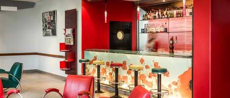 Una zona de bar con sillas y taburetes rojos, una barra con botellas y una pared con un diseño circular.