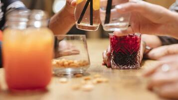 A group of people holding glasses with straws, a jar of nuts, and a glass of red drink on a table.