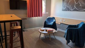 Ein Zimmer mit einem Flachbildfernseher, einem runden Tisch mit Büchern, einem Sessel und einem Sofa.