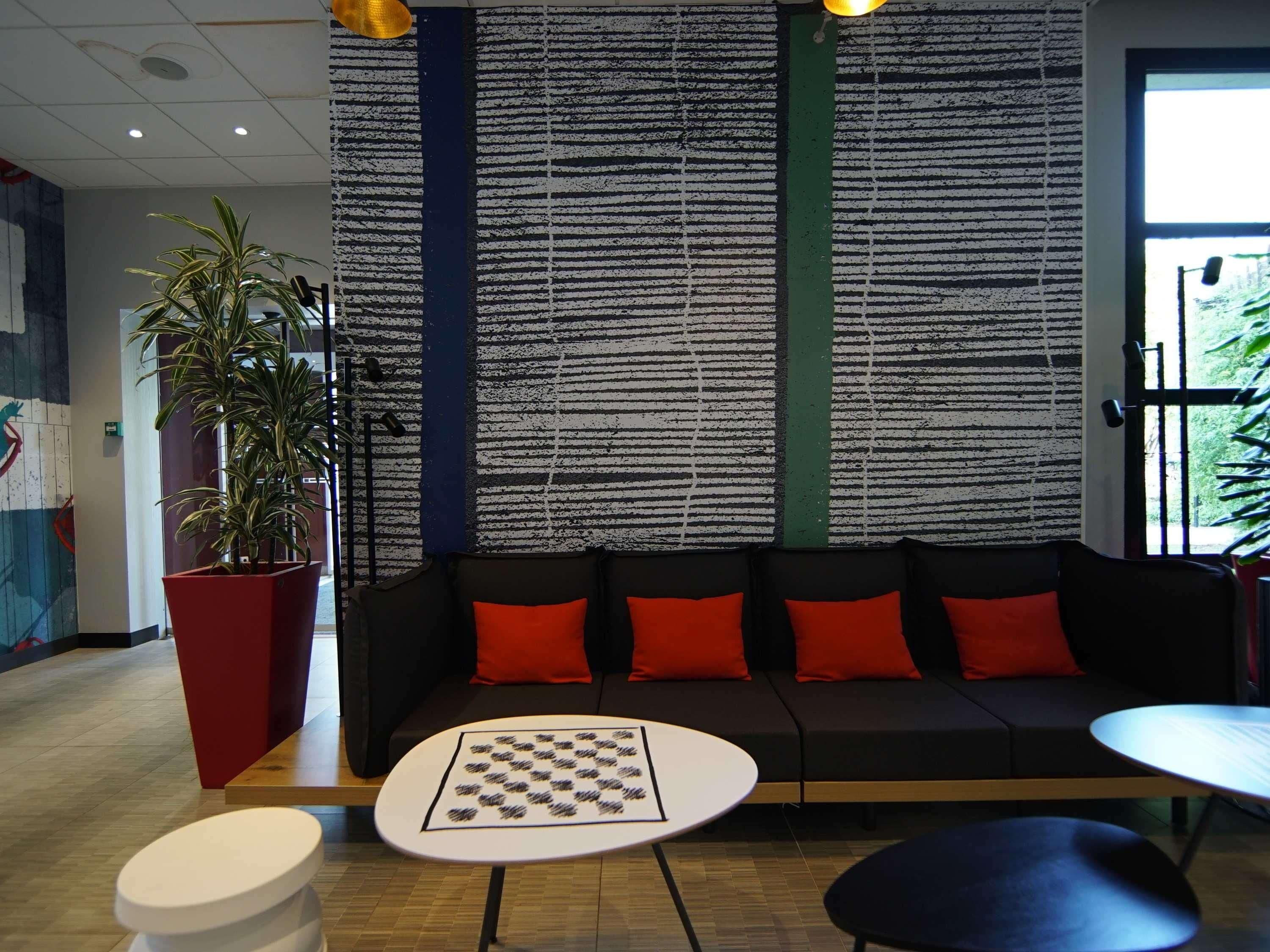 Un área de estar moderna con un sofá negro, cojines rojos, una mesa de ajedrez y una planta en maceta.