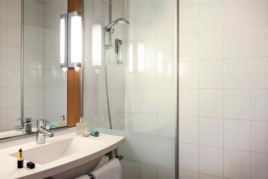 A bathroom with a sink, mirror, shower, and a towel rack.